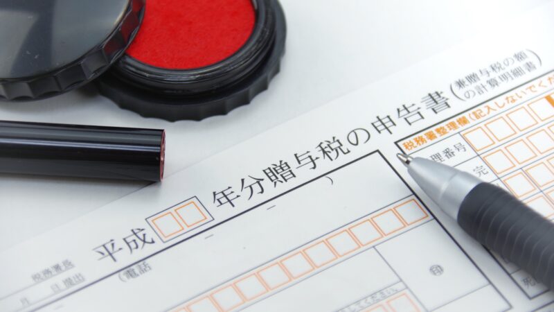 年分の贈与税申告書と朱肉、黒い印鑑、先端を申告書に向けたボールペンが並ぶデスクのクローズアップ