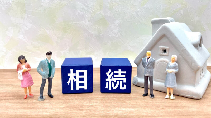 ミニチュアの家と、高齢夫婦・若い夫婦のフィギュアの間に「相続」と書かれた青いブロックが並んでいる様子