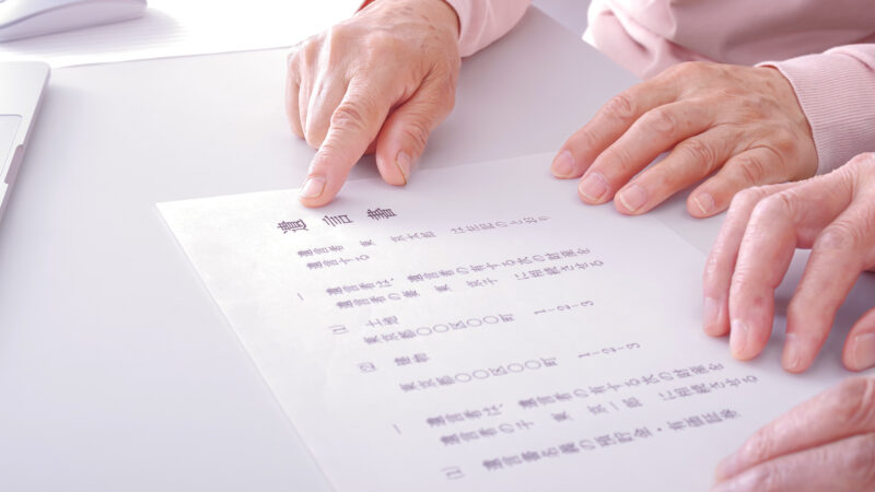 高齢夫婦が遺言書と財産目録の内容を指さしながら確認している手元のアップ