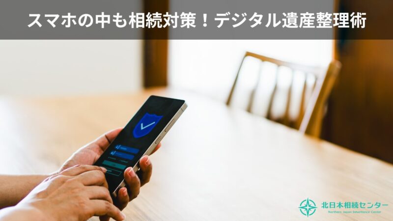スマホの画面にセキュリティマークが表示され、木目のテーブルの上で大人の手がスマホを操作している様子。画像上部に「スマホの中も相続対策！デジタル遺産整理術」の文字、右下に北日本相続センターのロゴが表示されているアイキャッチ画像。