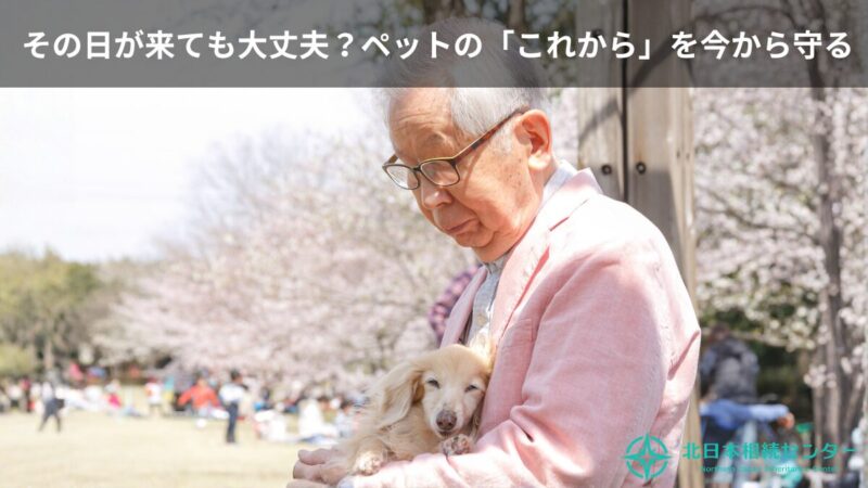 桜の咲く公園で、高齢の男性が小型犬をやさしく抱きしめている様子。「その日が来ても大丈夫？ペットの『これから』を今から守る」という文字と北日本相続センターのロゴ入り